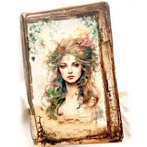 May include: A decorative book with a vintage aesthetic. The cover features a portrait of a woman with long, wavy hair adorned with flowers and leaves. The color palette includes greens, browns, and soft pastels, creating a whimsical and artistic feel.