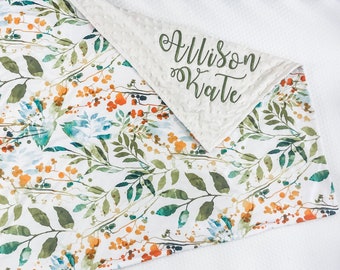 Puede incluir: Una manta de bebé blanca y verde con estampado floral y un respaldo de minky blanco. La manta está personalizada con el nombre "Allison Kate" en letras cursivas verdes.
