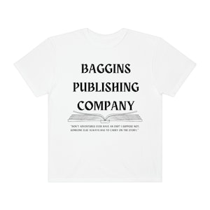 Op de afbeelding: Wit T-shirt met zwarte tekst die "Baggins Publishing Company" luidt en een zwart-witte illustratie van een open boek met de quote "Hebben avonturen ooit een einde? Ik denk het niet. Iemand anders moet het verhaal altijd voortzetten."