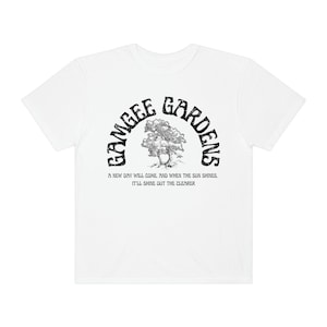 May include: White t-shirt with a black graphic print of a tree and the text "Gamgee Gardens" in a curved arch. The text below the graphic reads "A new day will come, and when the sun shines, it'll shine out the clearer."