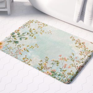 May include: A light blue bath mat with a floral pattern featuring pink and white flowers and green leaves. The mat has a watercolour-like effect.