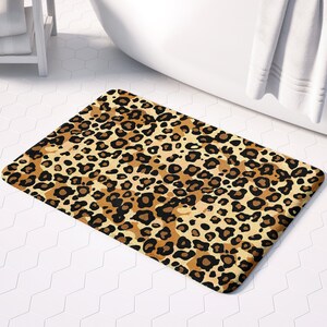 May include: A brown and black leopard print bath mat with a white bathtub and towel in the background.  Save for later.