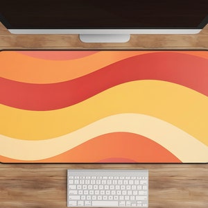 May include: A desk mat with a wavy pattern in shades of orange, yellow, and red. A white keyboard is on the desk below the mat.
