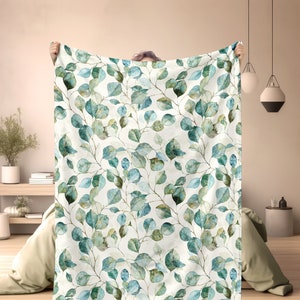May include: A white throw blanket with a watercolor pattern of green and blue eucalyptus leaves.