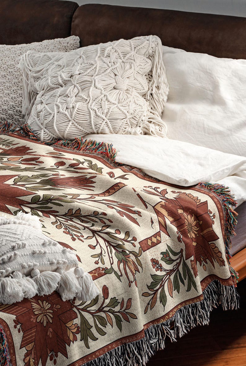 Puede incluir: Una manta crema con un estampado floral en tonos marrones y verdes, bordes con flecos y cojines decorativos. La manta est&aacute; colocada sobre una cama, creando un ambiente acogedor y atractivo.