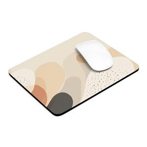 May include: A beige and brown abstract design mouse pad with a white computer mouse on top. The mouse pad has a black border and a subtle black polka dot pattern.