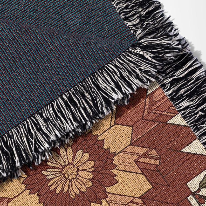 Puede incluir: Primer plano de una manta tejida con un patr&oacute;n floral y geom&eacute;trico. La manta presenta un tejido texturizado en color verde azulado y burdeos, con un borde con flecos en blanco y negro. La parte inferior muestra un dise&ntilde;o floral marr&oacute;n y beige.