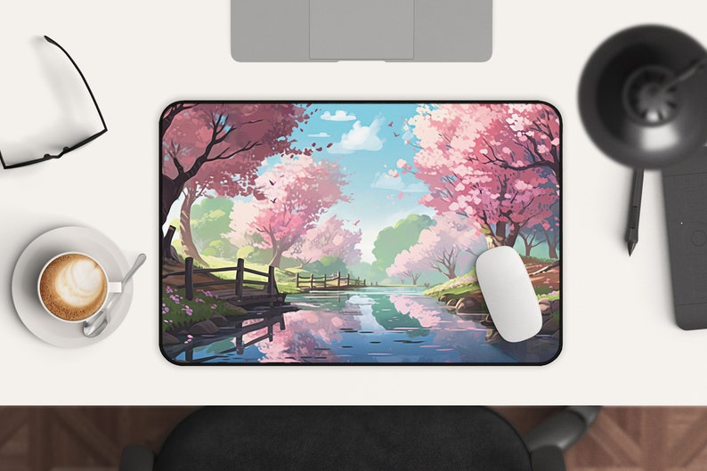 May include: A mouse pad with a scenic image of a river flowing through a forest with pink cherry blossom trees. The river reflects the trees and sky.