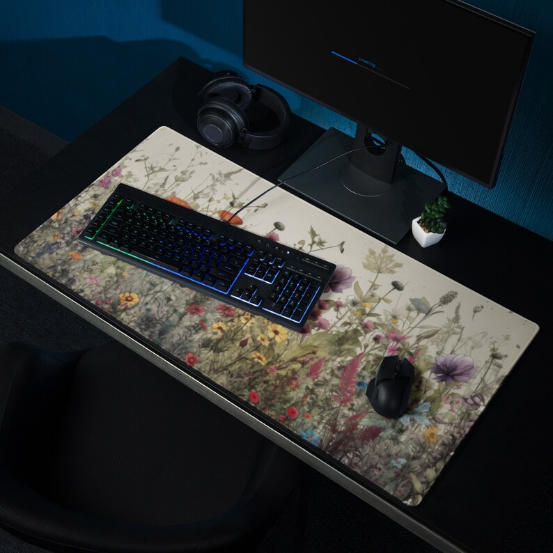 May include: A large, rectangular desk mat with a floral design featuring a variety of flowers and plants in shades of pink, purple, green, and yellow. A black keyboard with rainbow lighting and a black mouse are on the mat.