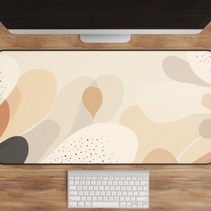 May include: A beige and brown abstract design desk mat with black dots. The mat is on a wooden desk with a white keyboard.