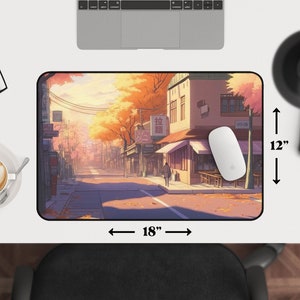 Op de afbeelding: Een kleurrijke anime-illustratie van een straatbeeld met gebouwen, bomen en mensen. De sc&egrave;ne speelt zich af in een stad met een straat die is omzoomd met winkels en restaurants. De gebouwen zijn in verschillende kleuren geschilderd, waaronder geel, oranje en rood. De bomen zijn een levendig groen en geel. De mensen lopen over straat en sommigen zitten aan tafels buiten de restaurants. De illustratie is geplaatst tegen een achtergrond van een helderblauwe lucht met witte wolken. De muismat is 45,7 cm breed en 30,5 cm hoog.