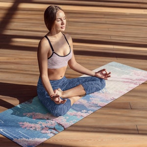 May include: A woman sits in a lotus position on a blue and pink yoga mat with a cherry blossom design. She is wearing a pink sports bra and blue yoga pants.