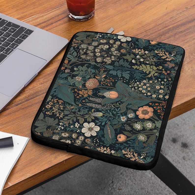 Pode incluir: Uma capa para laptop preta com um padr&atilde;o floral. O padr&atilde;o apresenta uma variedade de flores e folhas em tons de rosa, verde e branco sobre um fundo azul escuro.