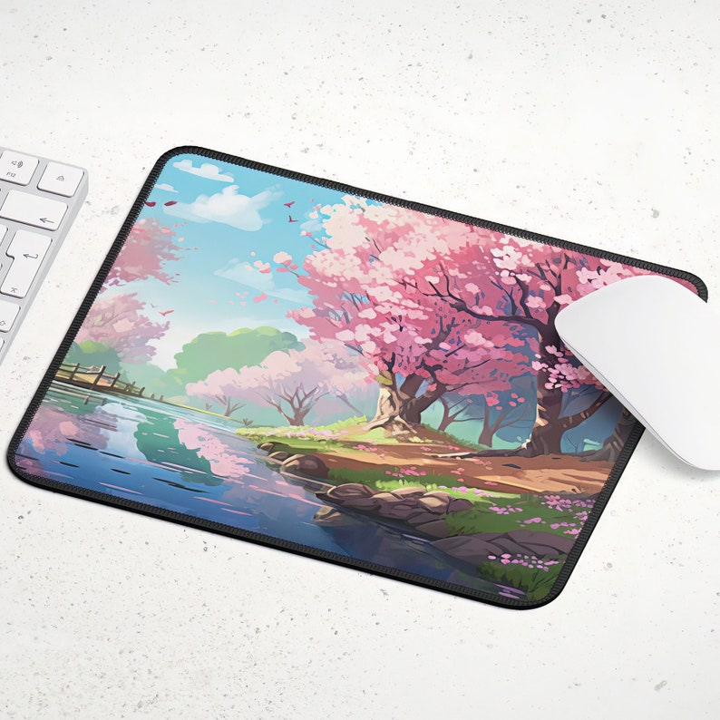 May include: A pink and blue mouse pad with a scenic image of a river flowing through a forest with cherry blossom trees. The trees are in full bloom and the river is reflecting the sky.