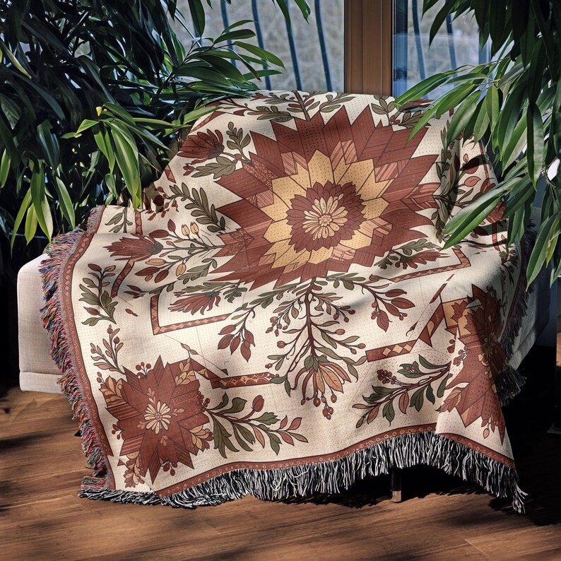 Puede incluir: Una manta decorativa con un estampado floral en tonos marr&oacute;n, beige y verde. La manta presenta un dise&ntilde;o central en forma de estrella y est&aacute; rematada con flecos en los bordes. La manta est&aacute; sobre una silla.