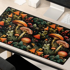 K&ouml;nnte beinhalten: Eine schwarze und gr&uuml;ne Mausmatte mit einem sich wiederholenden Muster aus orangefarbenen und roten Pilzen und gr&uuml;nen Bl&auml;ttern.