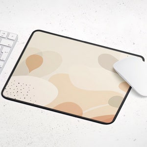 May include: A beige mouse pad with a black stitched border and an abstract design of beige and brown shapes. The mouse pad is on a white surface.
