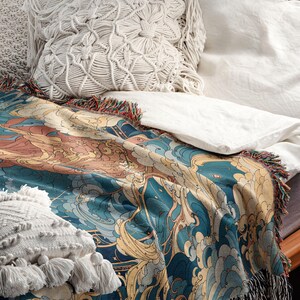 May include: A decorative throw blanket with a blue, gold, and peach wave pattern, fringed edges, and a soft texture. The blanket is draped over a bed with white linens and decorative pillows.