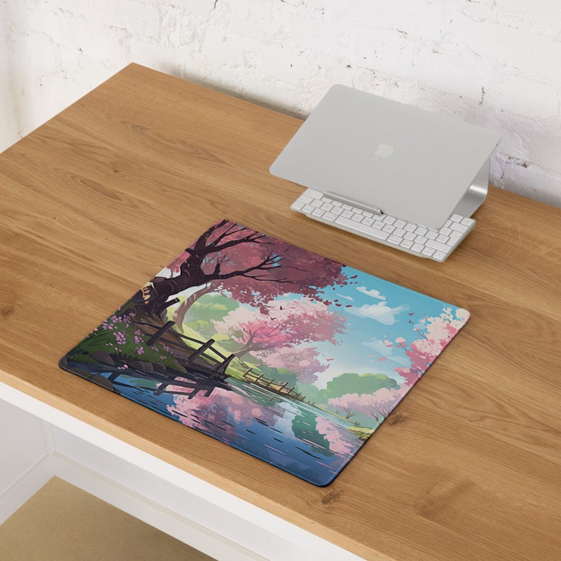 May include: A colorful mousepad with a scenic illustration of a river, a bridge, and trees with pink blossoms. The river reflects the trees and sky.