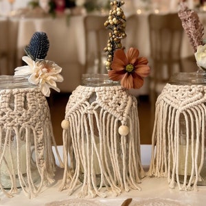 May include: Three glass jars with macrame covers and wooden beads. The jars are decorated with dried flowers and greenery.