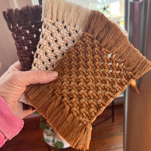 May include: Three crocheted coasters with fringe. The coasters are brown, beige, and a light brown color.