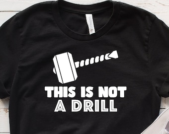 Peut inclure: T-shirt noir avec un graphique blanc d'un marteau et d'un foret avec le texte "Ceci n'est pas un exercice".