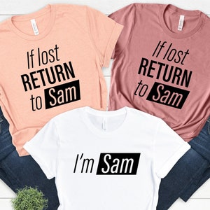 Könnte beinhalten: Drei T-Shirts mit passendem Design. Zwei Shirts sind pfirsichfarben und mauve mit dem Text "Wenn verloren, ZURÜCK zu Sam" in Schwarz. Das dritte Shirt ist weiß mit dem Text "Ich bin Sam" in Schwarz.