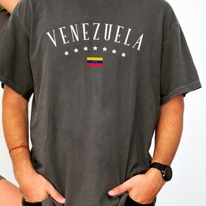 May include: A dark gray t-shirt with the word "VENEZUELA" printed in white with a small Venezuelan flag and stars.