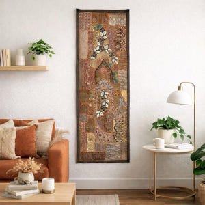May include: A tall, rectangular wall hanging featuring a patchwork of various brown, tan, and gold fabric segments. The textile displays intricate embroidery, beadwork, and sequin details arranged in geometric and floral patterns with a dark border.