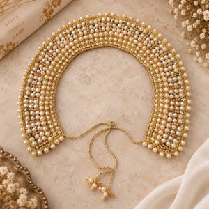 May include: A detachable collar crafted from gold-toned thread and densely embellished with cream-colored pearls and small clear crystals. The rounded collar features a delicate gold chain tie closure at the front, finished with two small pearl accents.