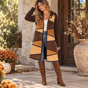 May include: A long-sleeved hooded cardigan featuring a patchwork design of dark brown and tan suede-like panels with visible dark stitching. The garment is worn over a white top and blue jeans, paired with knee-high brown suede boots.