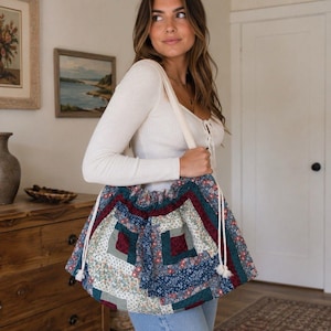 May include: A large, soft, quilted tote bag featuring a patchwork design of various floral and geometric patterns in shades of deep red, navy blue, sage green, and cream. The bag includes thick white rope shoulder straps and a drawstring closure.
