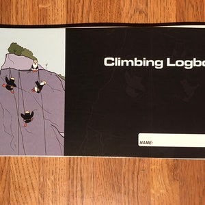 Puede incluir: Una portada ilustrada en blanco y negro de un cuaderno de registro de escalada en espiral. La portada presenta una caricatura de cuatro frailecillos descendiendo en rappel por un acantilado. El texto "Climbing Logbook" está impreso en blanco en la portada. Hay un espacio en blanco para un nombre.