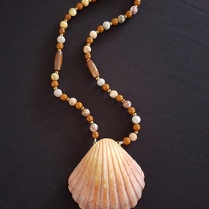 May include: A brown and white beaded necklace with a large seashell pendant. The necklace is made of natural stones and has a gold clasp.
