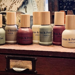 May include: A row of eight small glass bottles with bamboo lids. The bottles are labeled "Prim & Prickles" and have different scents, including unscented and vanilla.