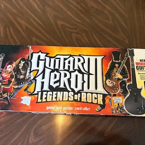 Peut inclure: Une boîte en carton rectangulaire pour le jeu vidéo PlayStation 3 Guitar Hero III Legends of Rock. L'emballage présente des graphismes orange et noirs, des illustrations de guitaristes, une guitare sans fil noire et le boîtier du jeu.
