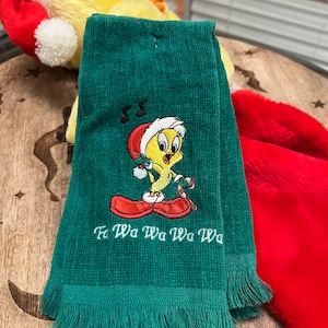 May include: Green kitchen towel with a fringed edge. It features an embroidered image of Tweety Bird wearing a Santa hat and holding a candy cane. The text "Fa Wa Wa Wa Wa" is embroidered below the image.