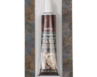 May include: A tube of Art Alchemy Antiquing Wax in the color Sepia, packaged on a rectangular cardboard backing. The tube features white text reading Antiquing Wax, Sepia, and 0.68 fl. oz. (20 ml). A dark brown wax swatch is visible below the packaging.