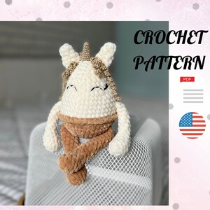 Könnte beinhalten: Häkelanleitung für ein weißes Einhorn-Amigurumi mit braunen Beinen und einem goldenen Horn. Das Muster ist als PDF-Download erhältlich. Das Bild enthält auch den Text "CROCHET PATTERN" und eine US-Flagge.