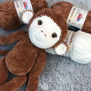 May include: A brown crocheted monkey toy with white facial features and brown yarn balls labeled "HIMALAYA DOLPHIN BABY" in the background.
