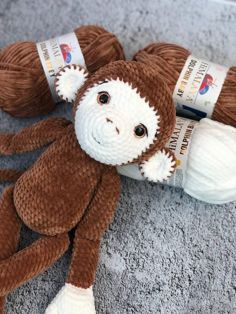 May include: A brown crocheted monkey toy with white facial features and brown yarn balls labeled "HIMALAYA DOLPHIN BABY" in the background.