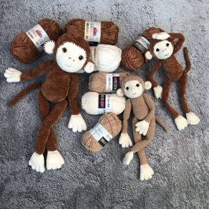 May include: Three brown crocheted monkey toys with white faces and yarn balls in various colors, including brown, beige, and white. The yarn balls have labels with the text "YarnArt Dolce Baby" and "HIMALAYA DOLPHINE BY".