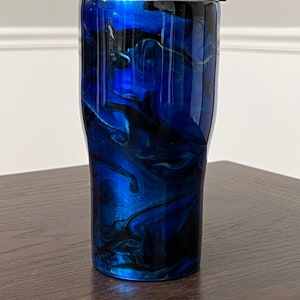 May include: A blue and black marbled stainless steel tumbler with a silver lid. The tumbler has a swirling pattern of blue and black paint.