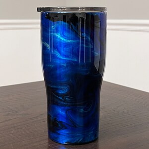 May include: A blue and black stainless steel tumbler with a swirl pattern. The tumbler has a lid.