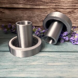 Peut inclure: Deux pi&egrave;ces imprim&eacute;es en 3D de couleur argent&eacute;e pour un projet de bricolage. Les pi&egrave;ces sont cylindriques et ont une finition lisse et m&eacute;tallique. Les pi&egrave;ces sont sur une surface en bois.