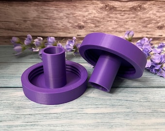 May include: Two purple plastic candle holders with a cylindrical design. The holders have a raised lip around the top and bottom.
