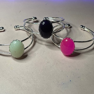 May include: Three silver bangle bracelets with different colored oval cabochons. The cabochons are black, white, and pink.