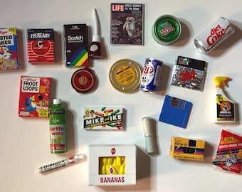May include: A collection of vintage miniature items, including cereal boxes, candy bars, a film reel, a can of STP motor oil, a cassette tape, a floppy disk, a can of Diet Coke, a box of bananas, a roll of film, a bottle of Turtle Wax, a box of Dum Dum Pops, a can of Krazy Glue, a bottle of Windex, a box of Eveready batteries, a VHS tape, a box of Frosted Flakes, a box of Fruit Loops, and a magazine cover of Life magazine featuring a photo of an astronaut.