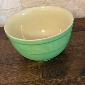 Puede incluir: Un cuenco mezclador redondo con un exterior de color verde claro y un interior de color crema. El exterior presenta un patrón texturizado que consiste en líneas verticales y detalles circulares en relieve alrededor de la parte superior.