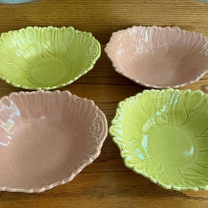 May include: A set of four ceramic bowls featuring a molded leaf design along the edges. Two bowls are light green and two bowls are a soft pink color. Each bowl has a smooth, glossy finish and a scalloped rim that mimics the shape of a leaf.
